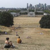 People sit on the parched grass in Greenwich Park with the National Maritime Museum and Canary Wharf financial district in the background in London, England, on July 17, 2022.