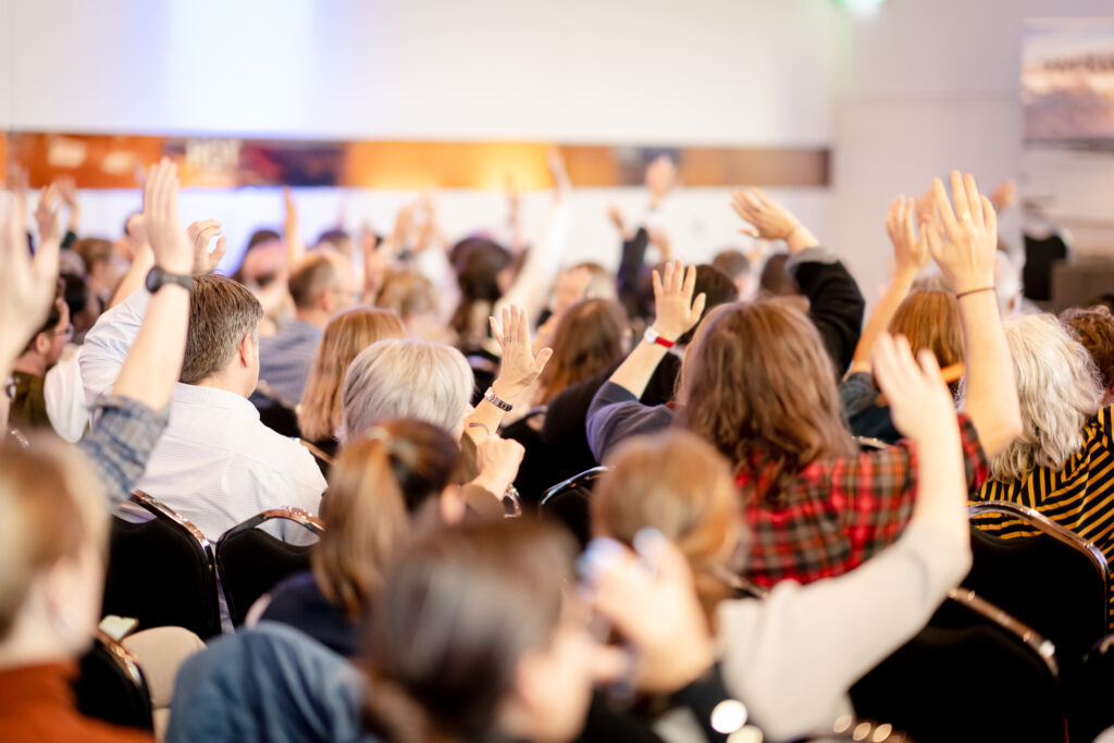 Attendees at the MACC Hub conference raise their hands during a plenary session in the main room.