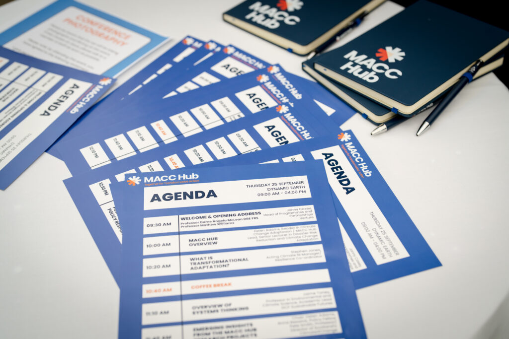 MACC Hub branded notebooks, pens and conference agenda arranged on a table.